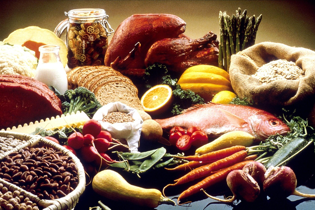 A table of fresh food: a bottle of milk, roast turkey, beef, a whole fish, bread, carrots, beets and other vegetables